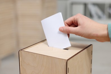 Photo of Woman putting her vote into ballot box on blurred background, closeup