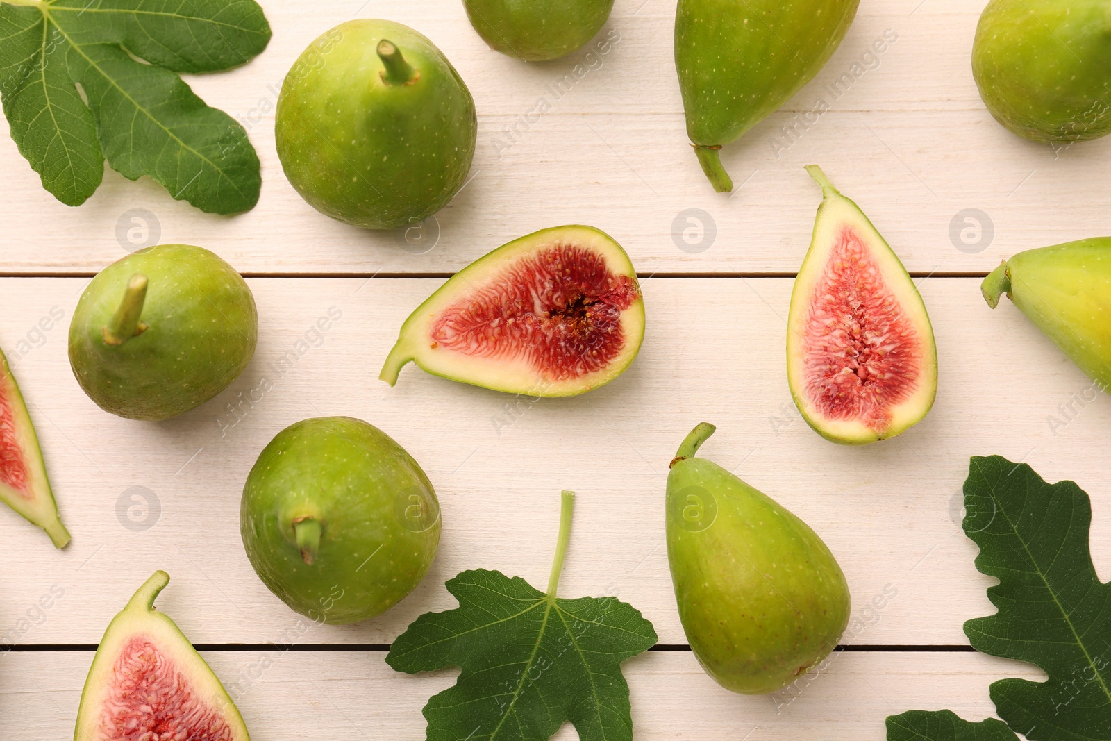 Photo of Cut and whole green figs with leaves on white wooden table, flat lay