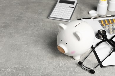 Photo of Piggy bank, stethoscope, calculator, clipboard and pills on light grey table, space for text. Medical insurance