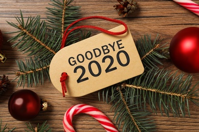 Photo of Tag with text Goodbye 2020 and festive decor on wooden background, flat lay