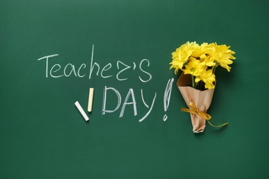 Flat lay composition with flowers and inscription TEACHER'S DAY on green chalkboard