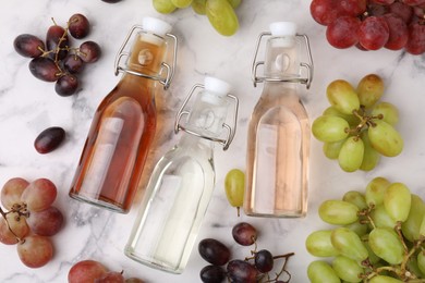 Different types of vinegar in bottles and grapes on light marble table, flat lay