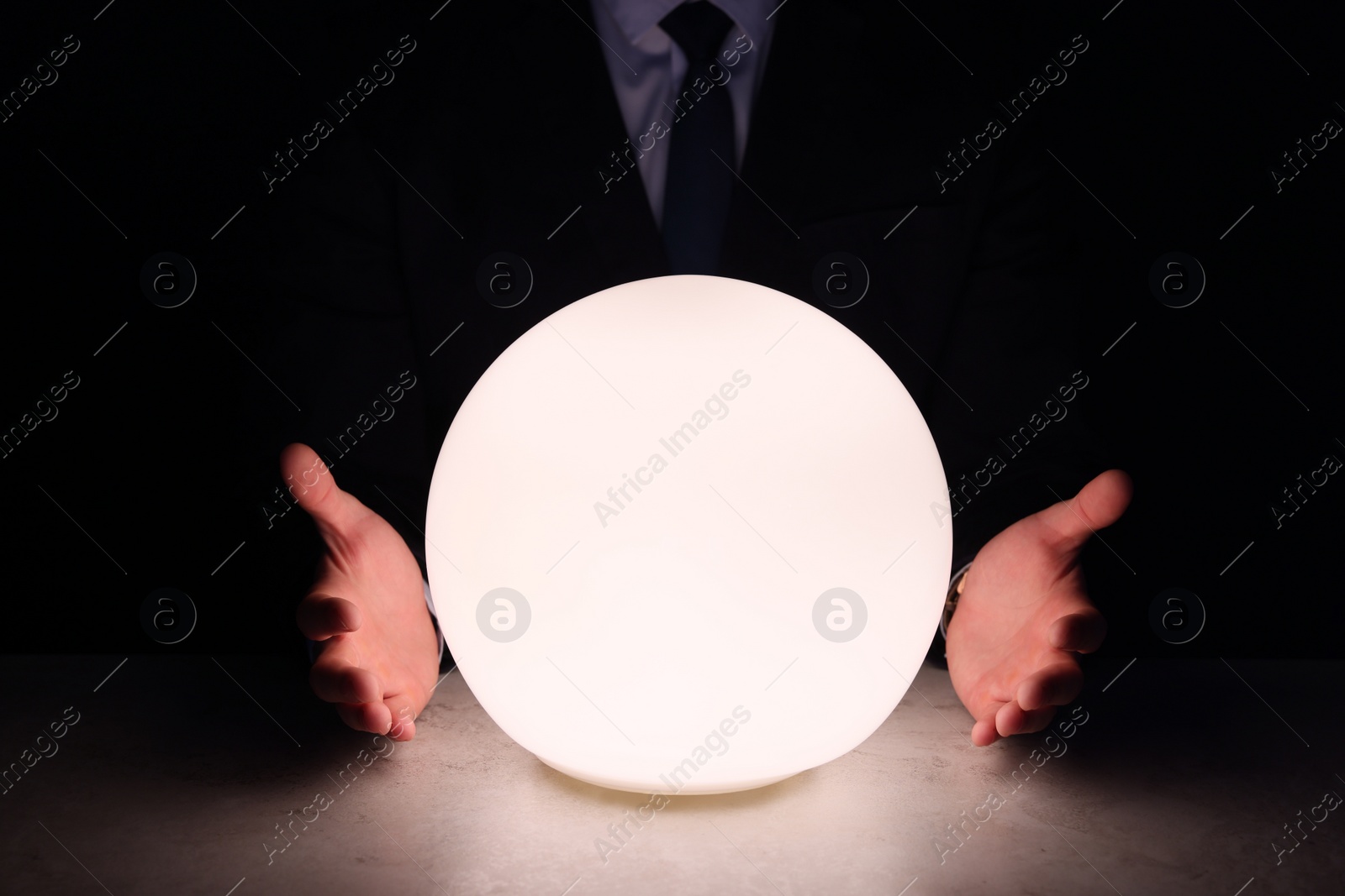 Photo of Businessman using glowing crystal ball to predict future at table in darkness, closeup. Fortune telling