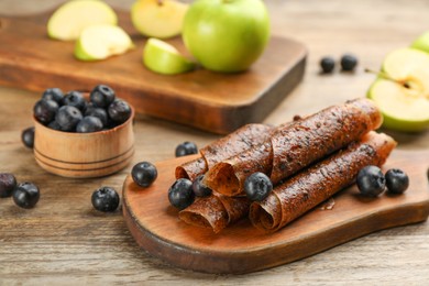 Photo of Composition with delicious fruit leather rolls and blueberries on wooden table