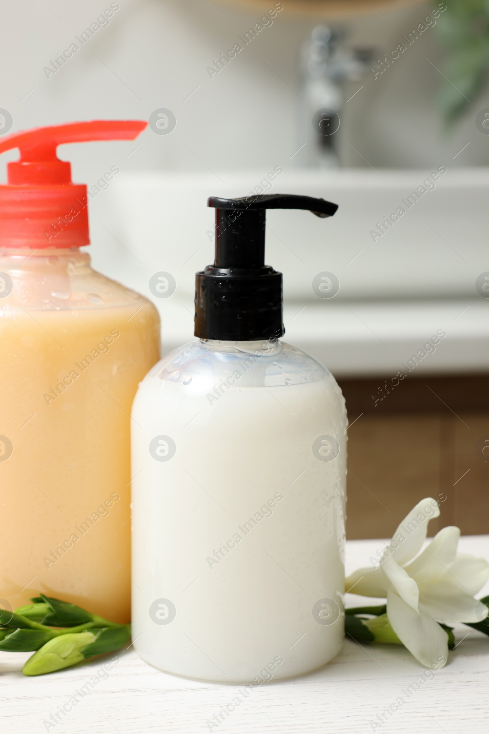 Photo of Dispensers of liquid soap and freesia flower on white table in bathroom