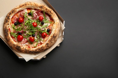 Photo of Tasty pizza with meat and arugula in cardboard box on black background, top view. Space for text