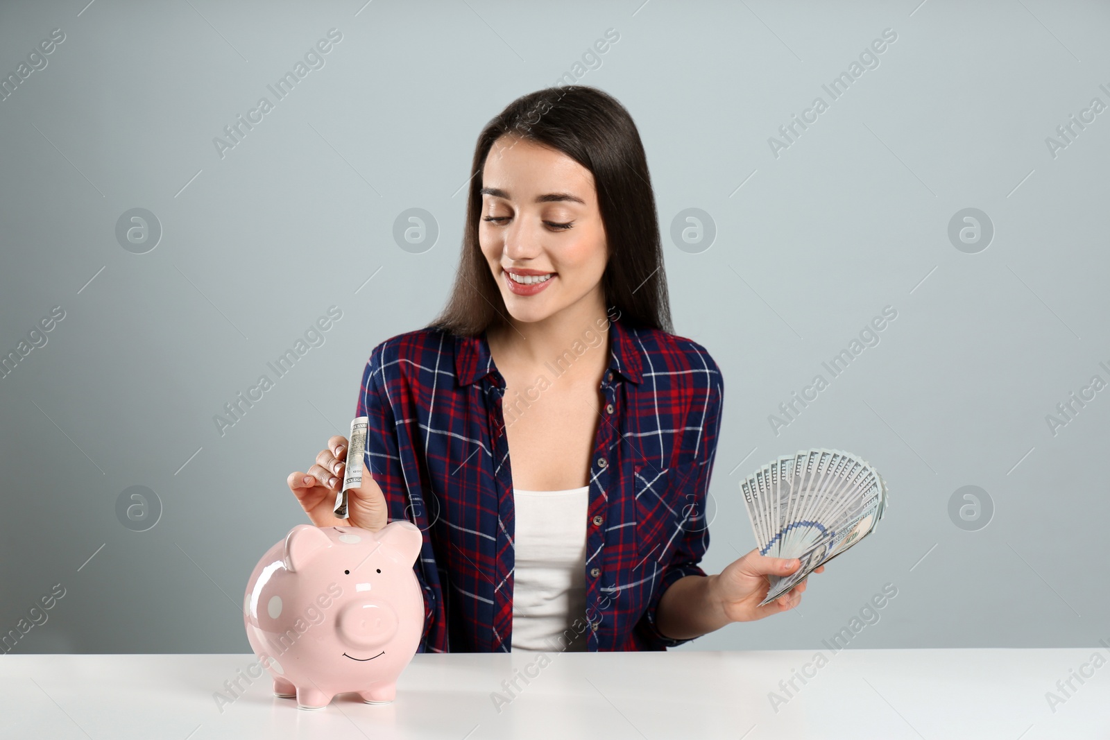 Photo of Young woman putting money into piggy bank at table on light grey background