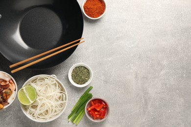 Photo of Flat lay composition with black wok, spices and products on grey textured table. Space for text