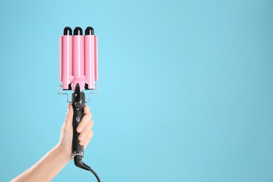 Photo of Woman holding triple curling hair iron on light blue background, closeup. Space for text