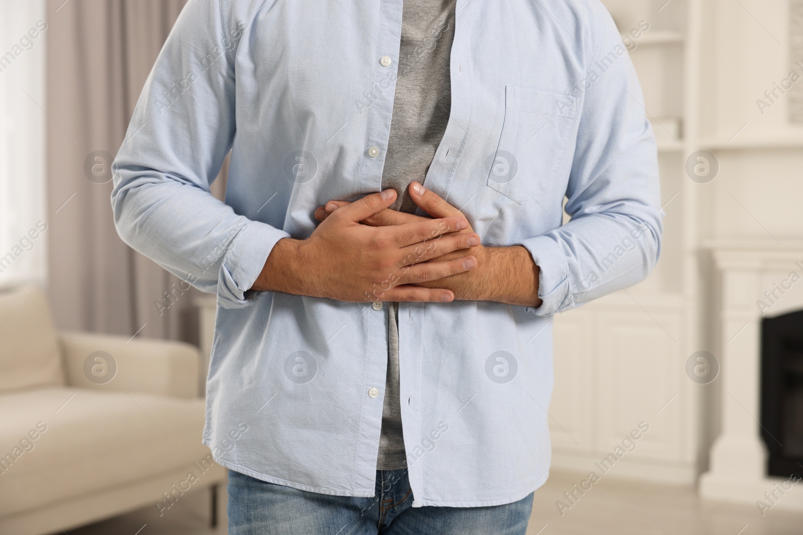 Photo of Young man suffering from stomach pain indoors, closeup