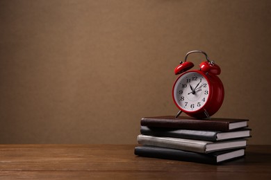 Photo of Alarm clock and stack of notebooks on wooden table against brown background, space for text. Time management
