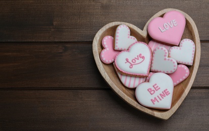 Delicious heart shaped cookies in bowl on wooden table, top view with space for text. Valentine's Day