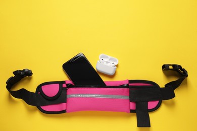 Photo of Stylish pink waist bag with smartphone and earphones on yellow background, flat lay. Space for text