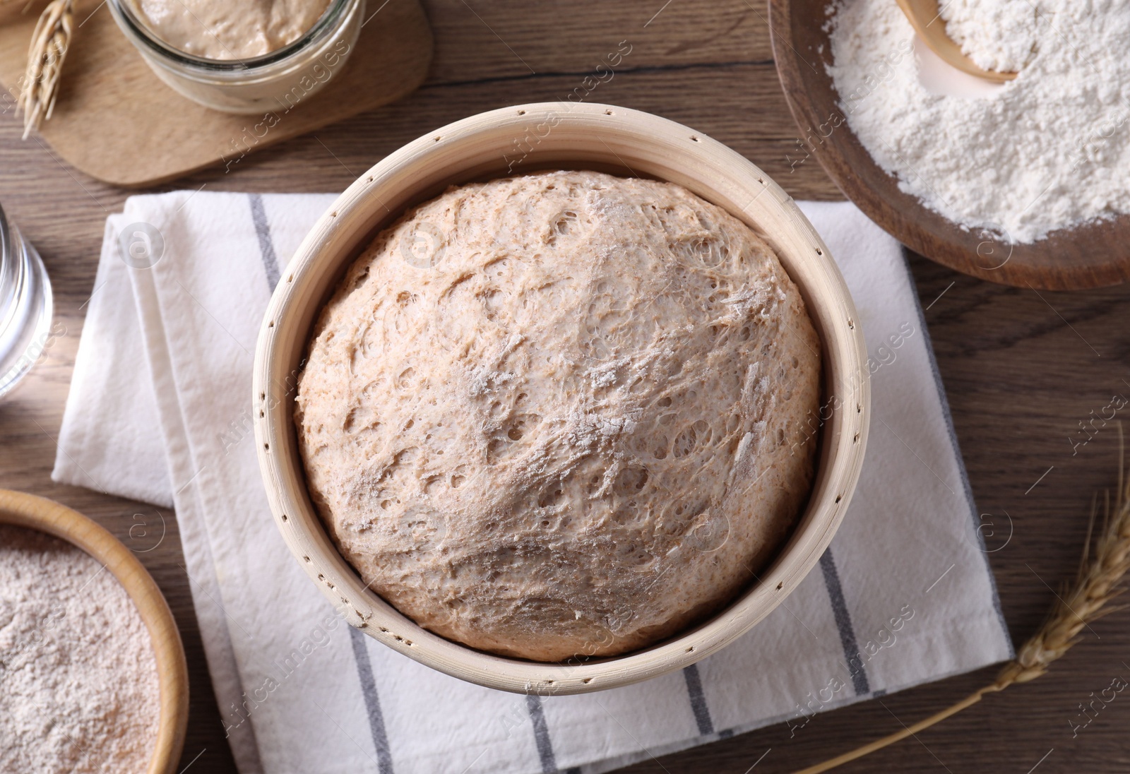 Photo of Fresh sourdough in proofing basket, flour and spikes on wooden table, flat lay