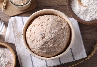 Fresh sourdough in proofing basket, flour and spikes on wooden table, flat lay