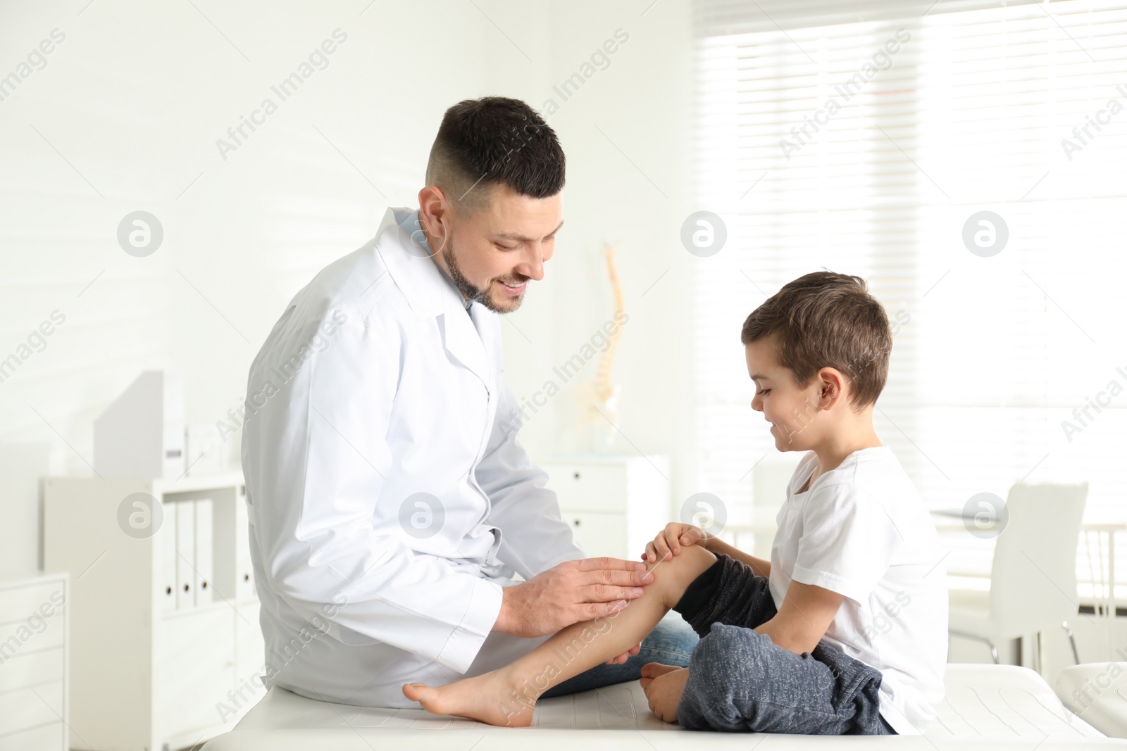 Photo of Professional orthopedist examining little patient's leg in clinic