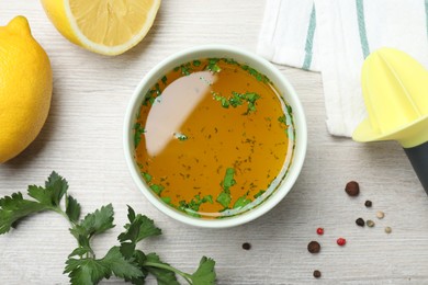 Photo of Bowl with lemon sauce and ingredients on white wooden table, flat lay. Delicious salad dressing