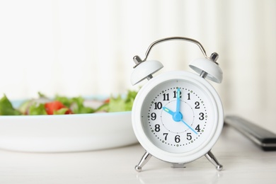 Photo of Alarm clock and plate with salad on white table. Meal timing concept