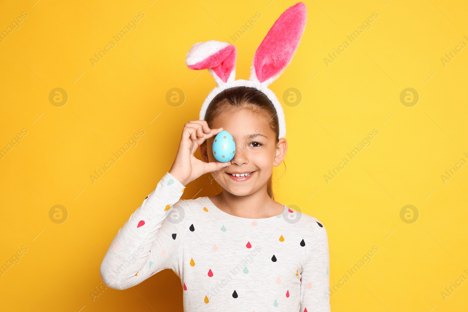 Photo of Cute happy girl with bunny ears and Easter egg against yellow background