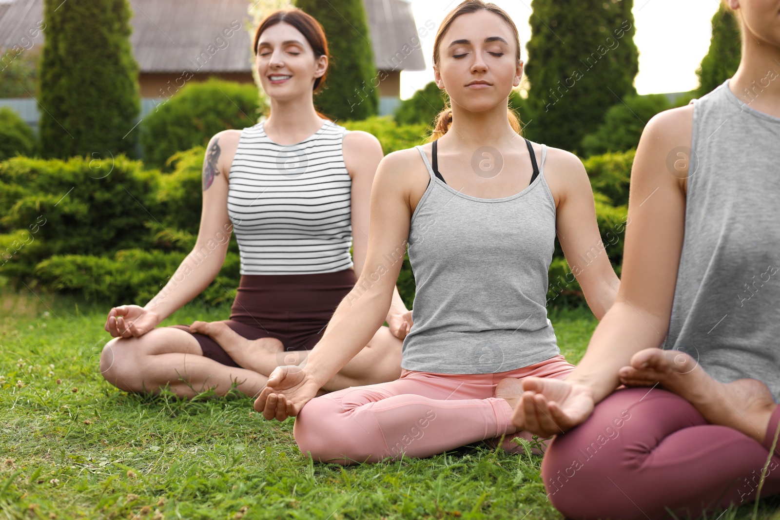 Photo of Young women meditating on green grass outdoors. Morning yoga