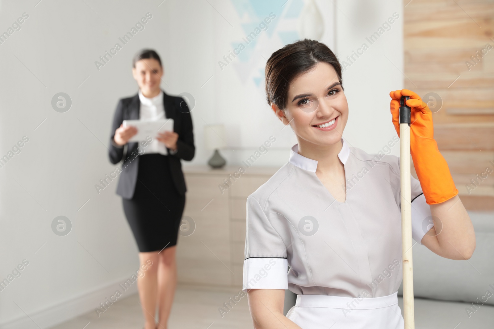 Photo of Young maid with mop and housekeeping manager in hotel room