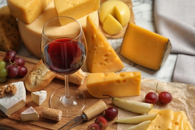 Photo of Board with different kinds of delicious cheese, snacks and wine on marble table