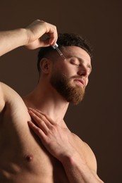 Photo of Handsome man applying serum onto his face on brown background, low angle view
