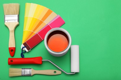 Photo of Can of orange paint, roller, brushes and color palette samples on green background, flat lay. Space for text