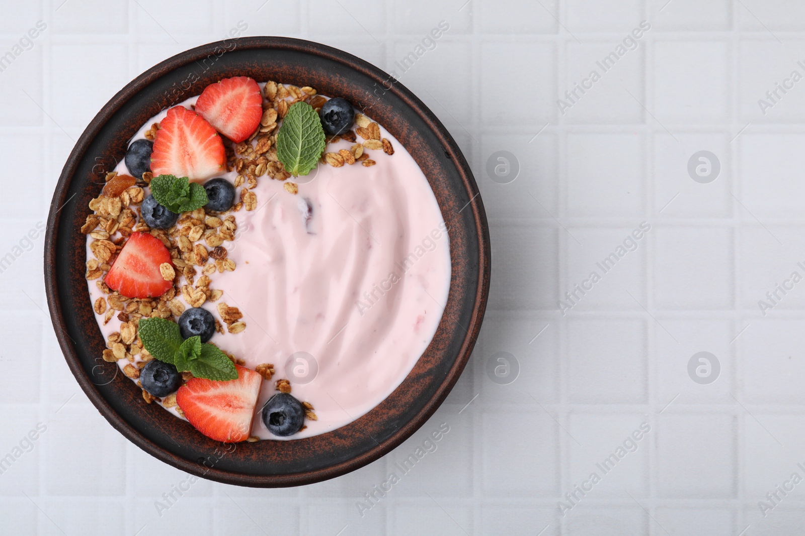 Photo of Bowl with yogurt, berries and granola on white tiled table, top view. Space for text