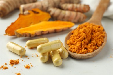 Photo of Aromatic turmeric powder, pills and raw roots on white table, closeup