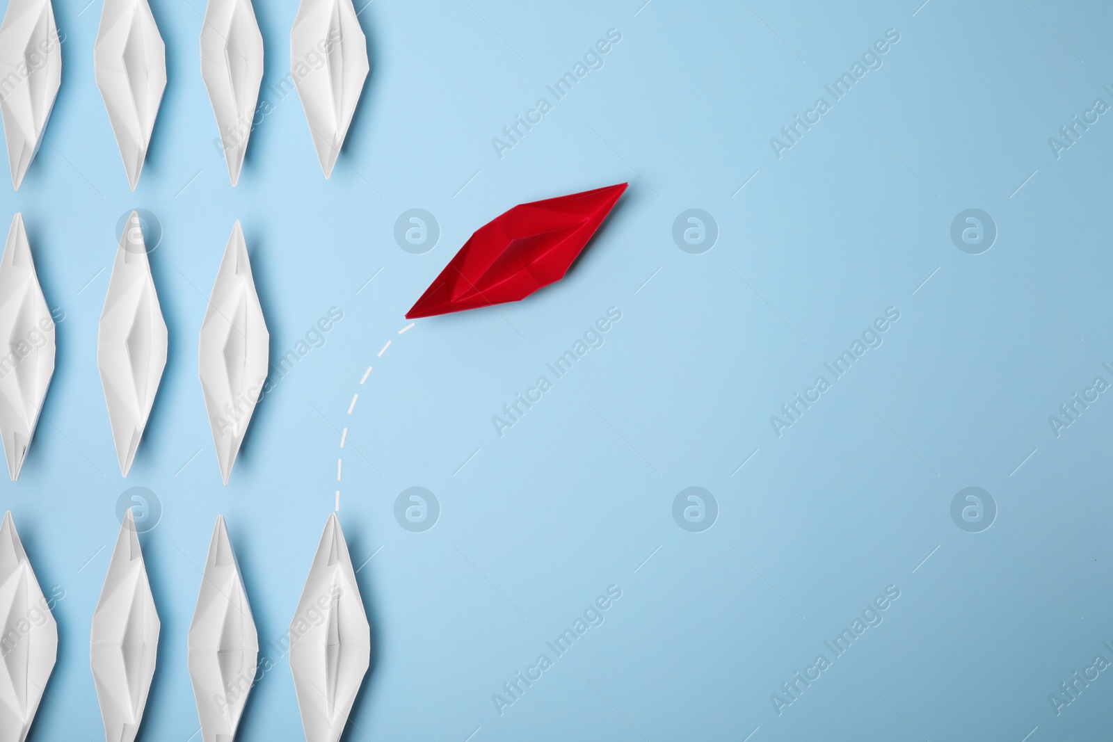 Photo of Red paper boat floating away from others on light blue background, flat lay with space for text. Uniqueness concept