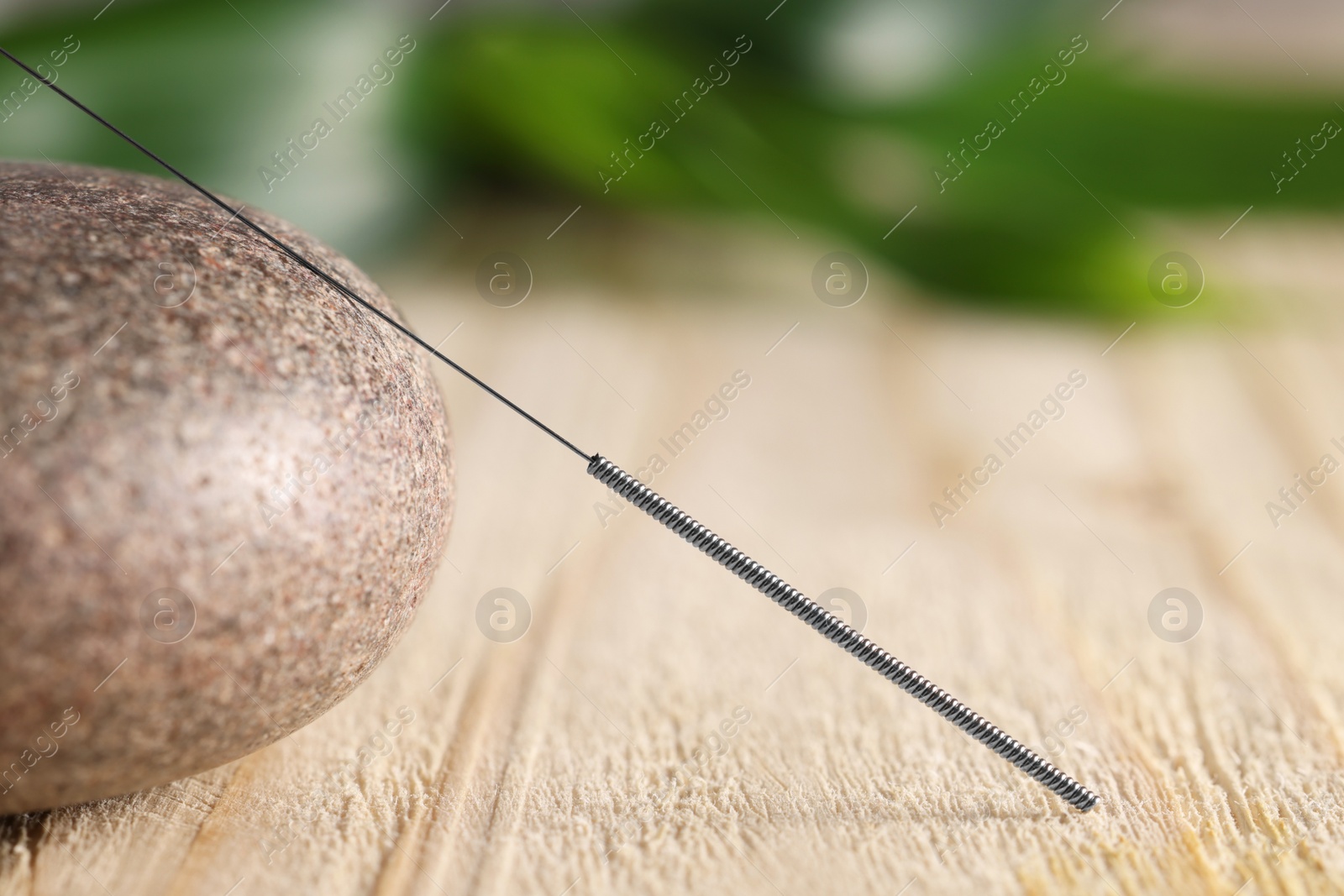 Photo of Acupuncture needle and spa stone on wooden table, closeup