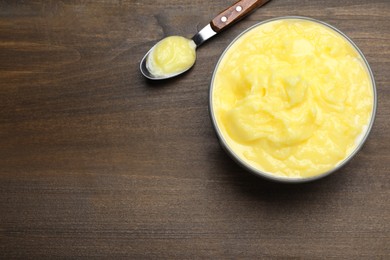 Bowl and spoon of Ghee butter on wooden table, flat lay. Space for text