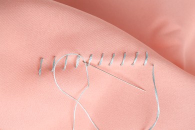 Photo of Sewing needle with thread and stitches on coral cloth, top view