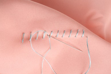 Sewing needle with thread and stitches on coral cloth, top view