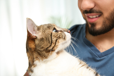 Photo of Happy man with cat at home, closeup. Friendly pet
