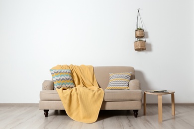 Photo of Cozy living room interior with sofa, pillows and plaid near light wall. Space for text
