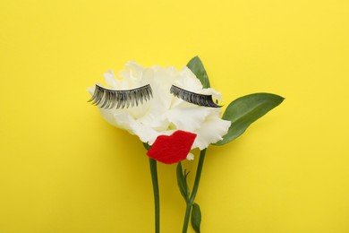 Photo of Flower with false eyelashes and red lips as beautiful face on yellow background, top view