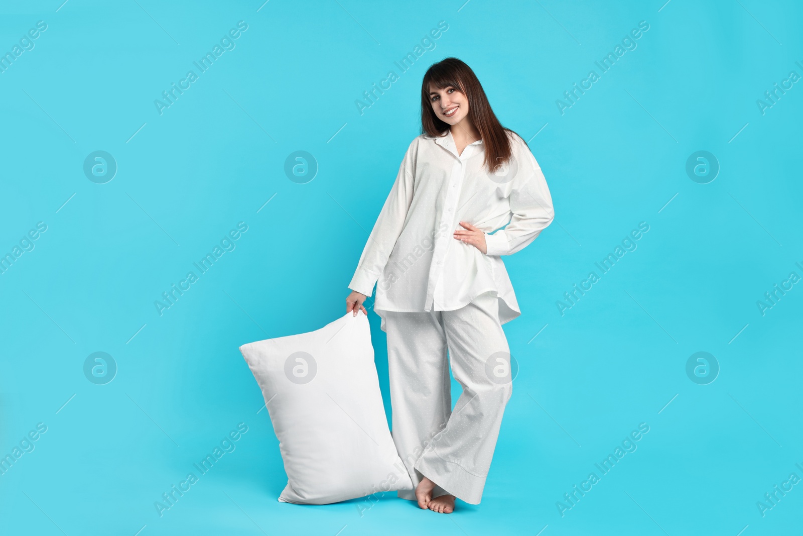 Photo of Happy woman in pyjama holding pillow on light blue background
