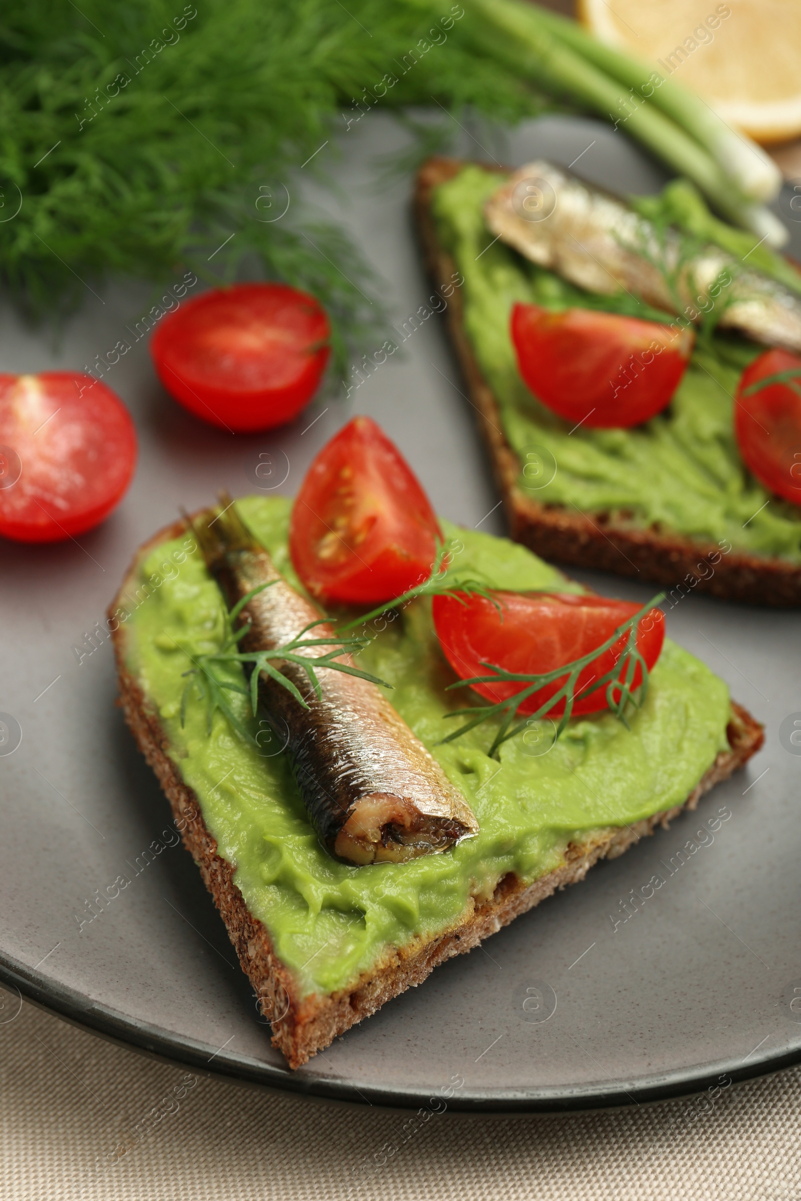 Delicious sandwiches with sprats, tomatoes, avocado puree and dill on table, closeup Photo of Delicious sandwiches with sprats, tomatoes, avocado puree and dill on table, closeup