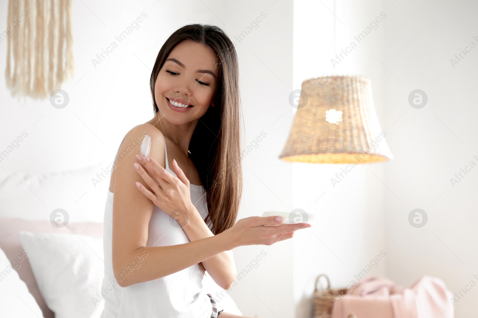 Photo of Beautiful young woman applying body cream in bedroom