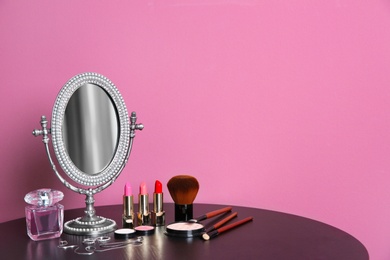 Photo of Stylish mirror, makeup products and accessories on table near color wall