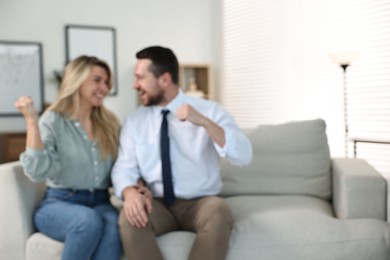 Photo of Blurred view of happy couple sitting on sofa at home, space for text