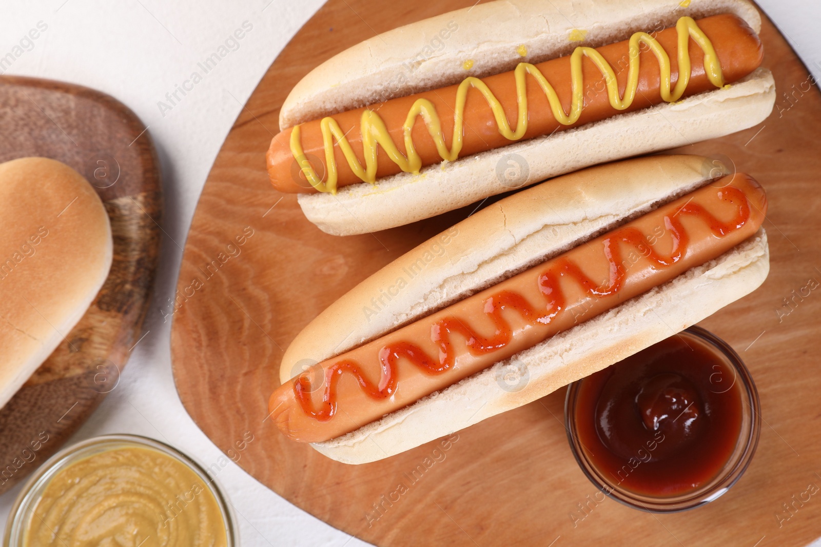 Photo of Tasty hot dogs with ketchup and mustard on white table, flat lay