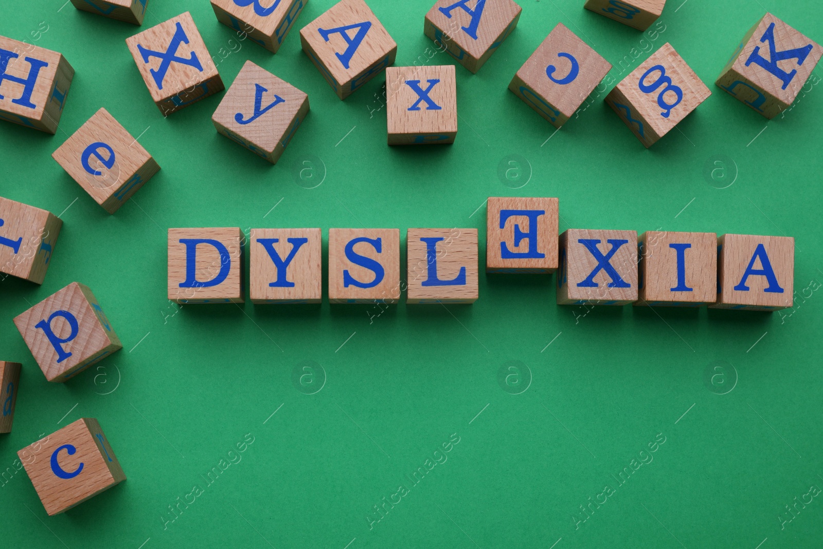 Photo of Word Dyslexia with inverted letter E of wooden cubes on green background, flat lay