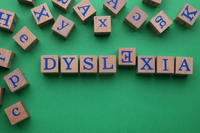 Word Dyslexia with inverted letter E of wooden cubes on green background, flat lay