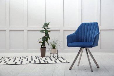 Modern blue armchair and beautiful houseplants near white wall indoors. Space for text