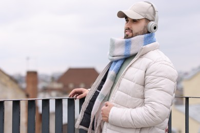 Photo of Handsome man in warm scarf and headphones outdoors. Space for text