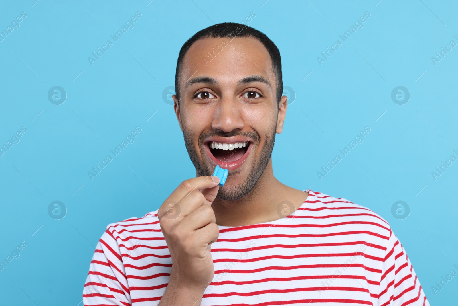 Photo of Portrait of happy young man with bubble gum on light blue background