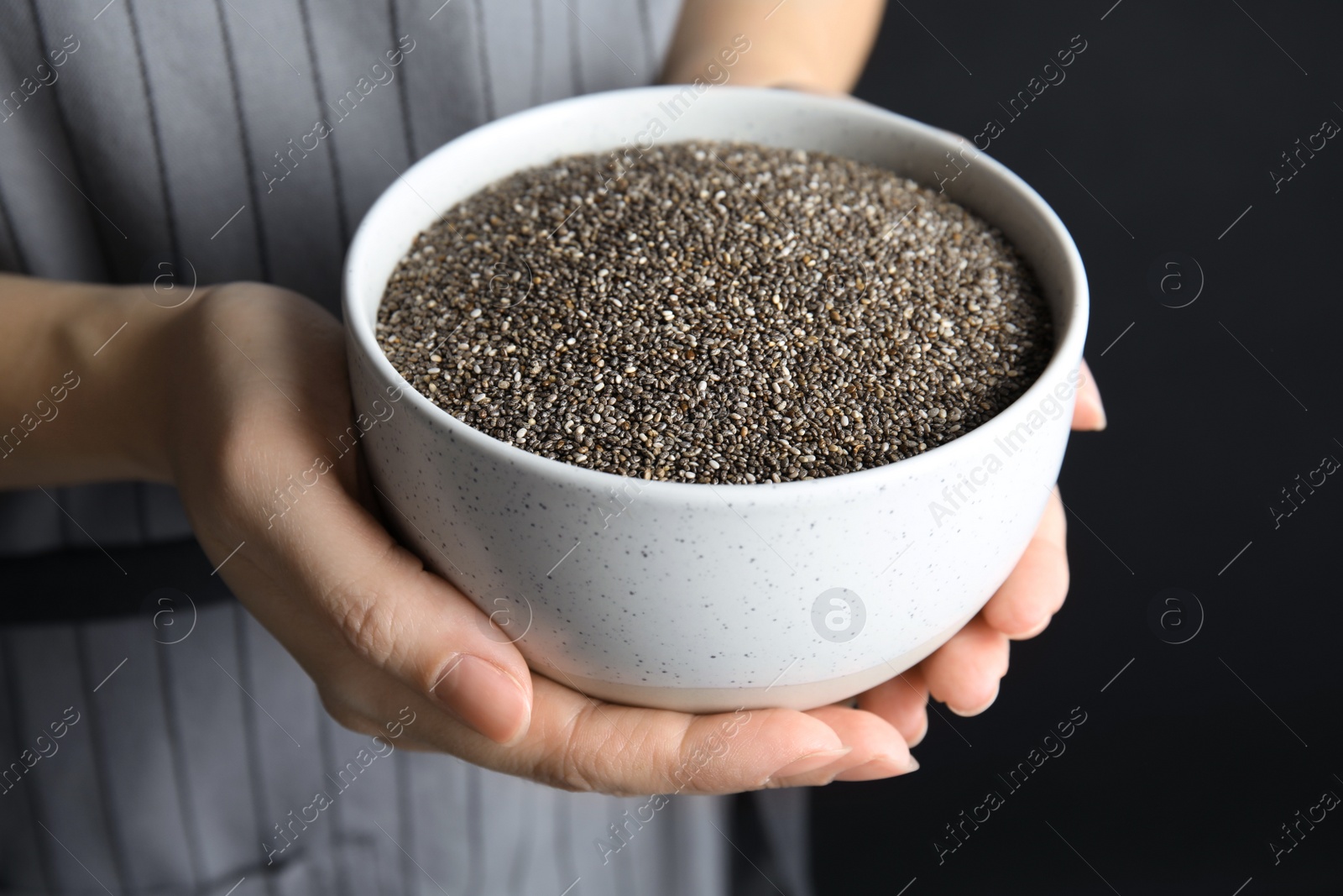 Photo of Woman holding bowl with chia seeds on dark background, closeup